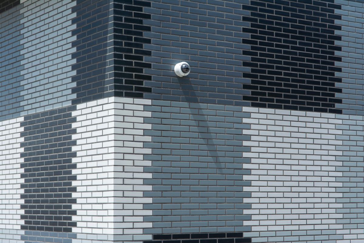 Grayscale facade featuring geometric brick pattern and surveillance camera, modern architecture.