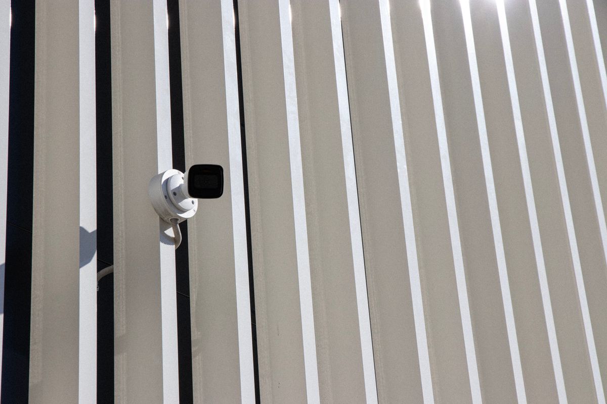 A security camera is mounted on a building with sleek, vertical lines creating a minimalist architectural effect.