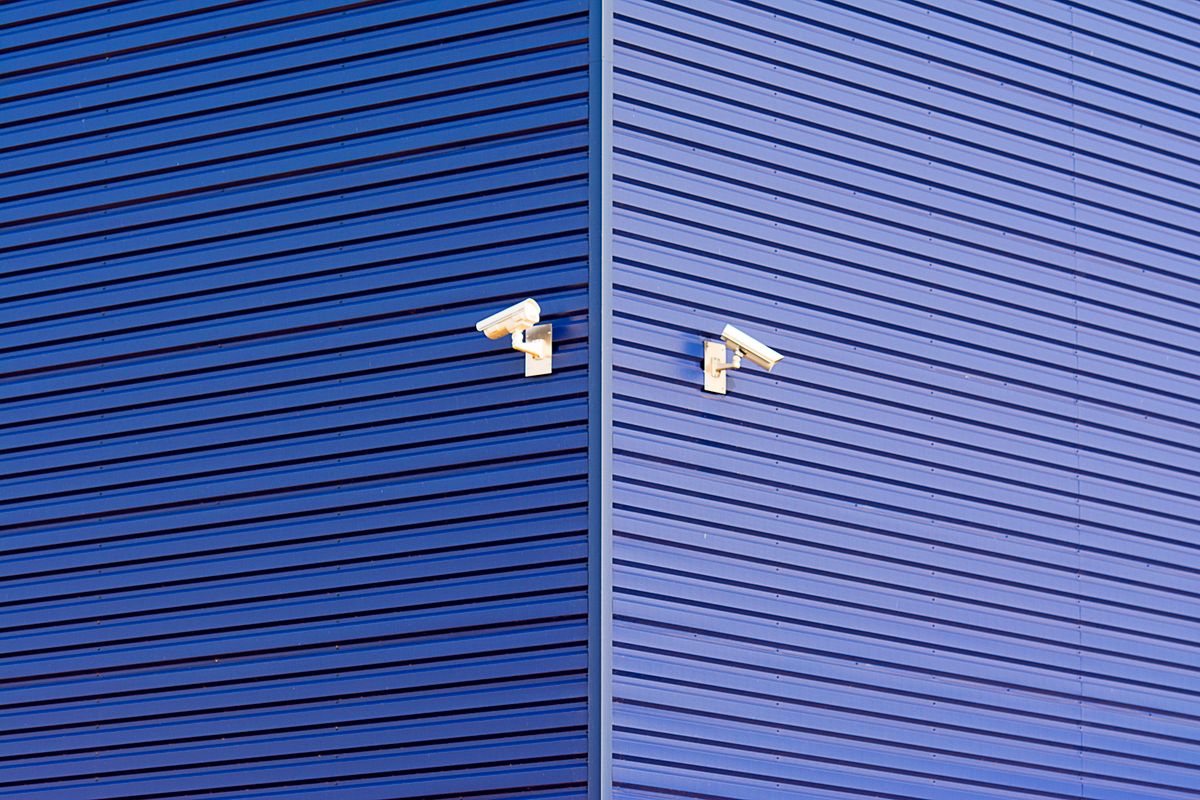 Minimalist image of a blue wall with two CCTV cameras emphasizing security and technology.