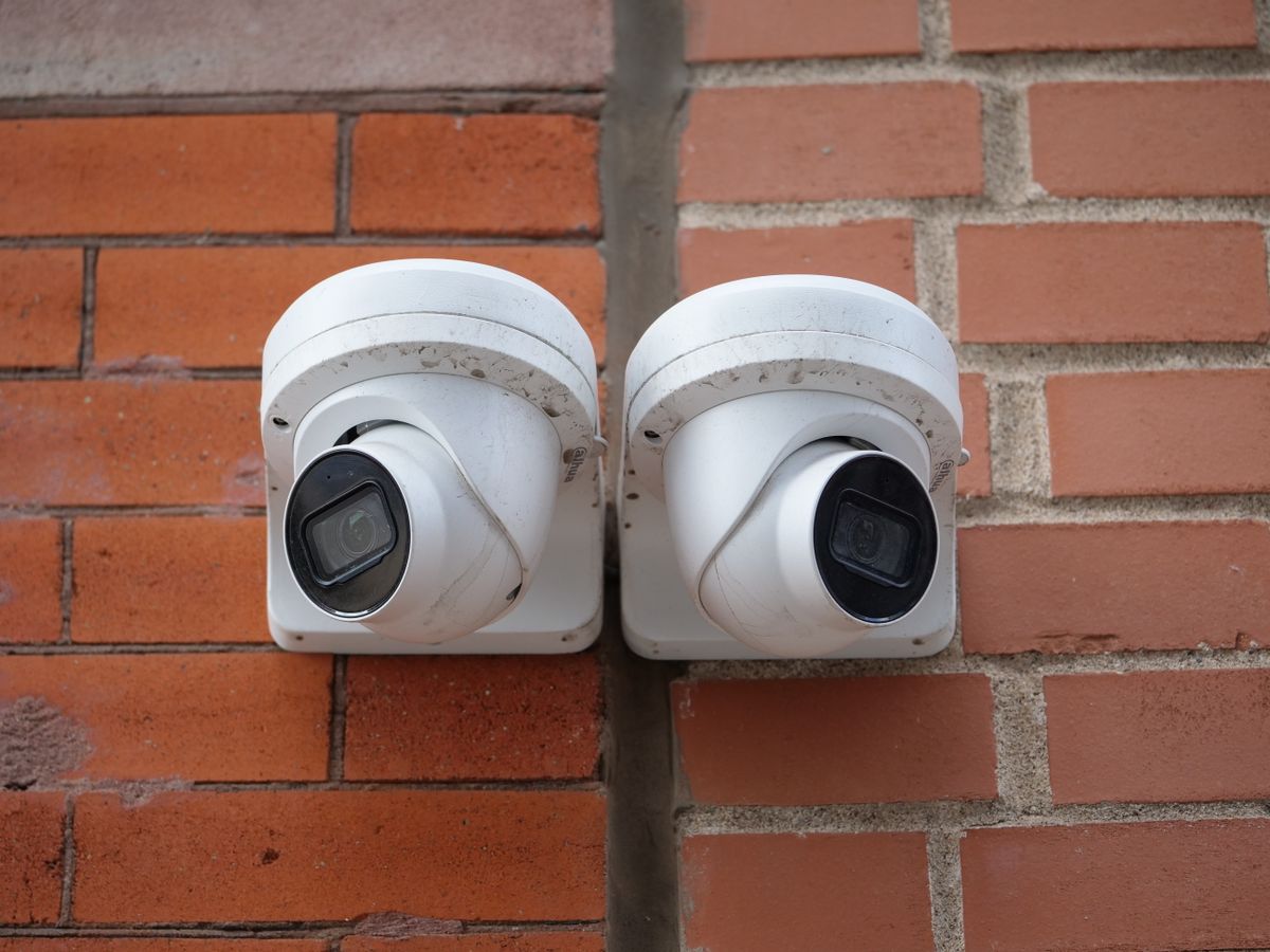 Two white dome security cameras mounted on a brick wall for urban surveillance.
