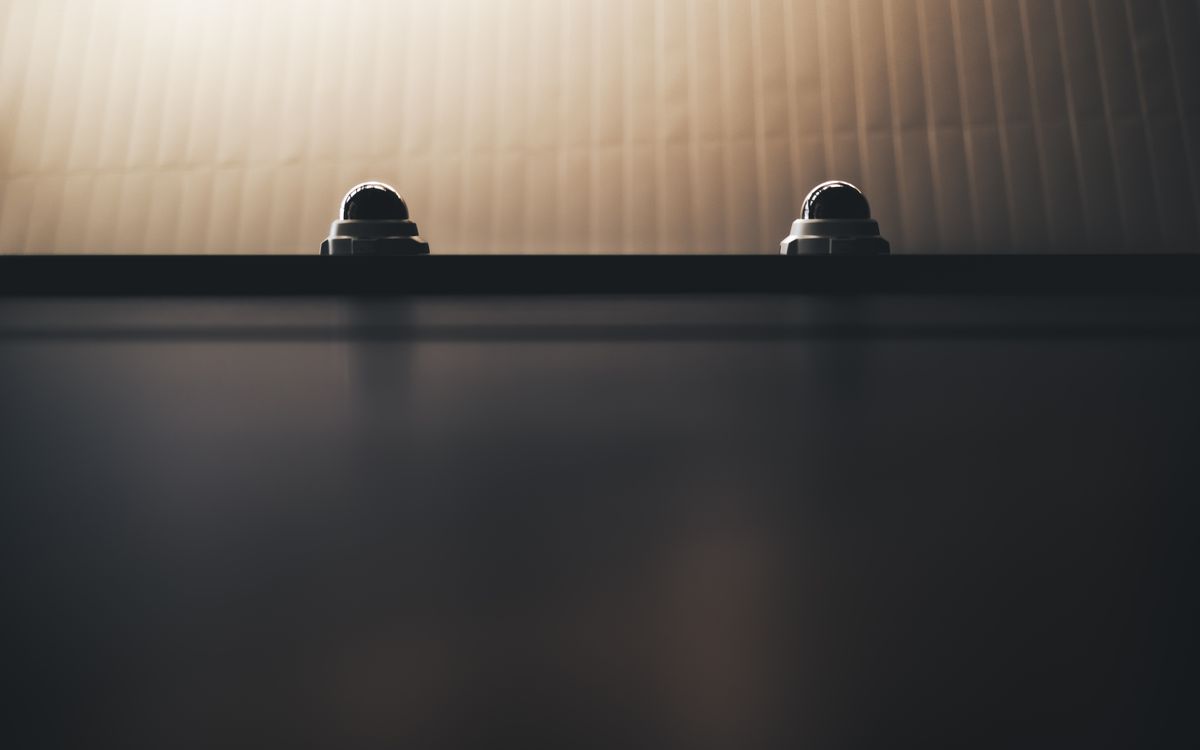 Two dome security cameras on a wall in dim lighting, emphasizing surveillance.