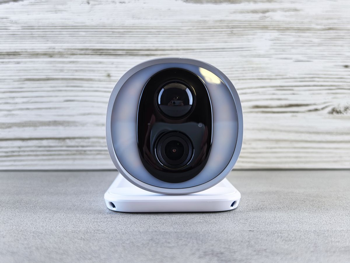 Close-up of a smart security camera with a modern design on a gray surface indoors.