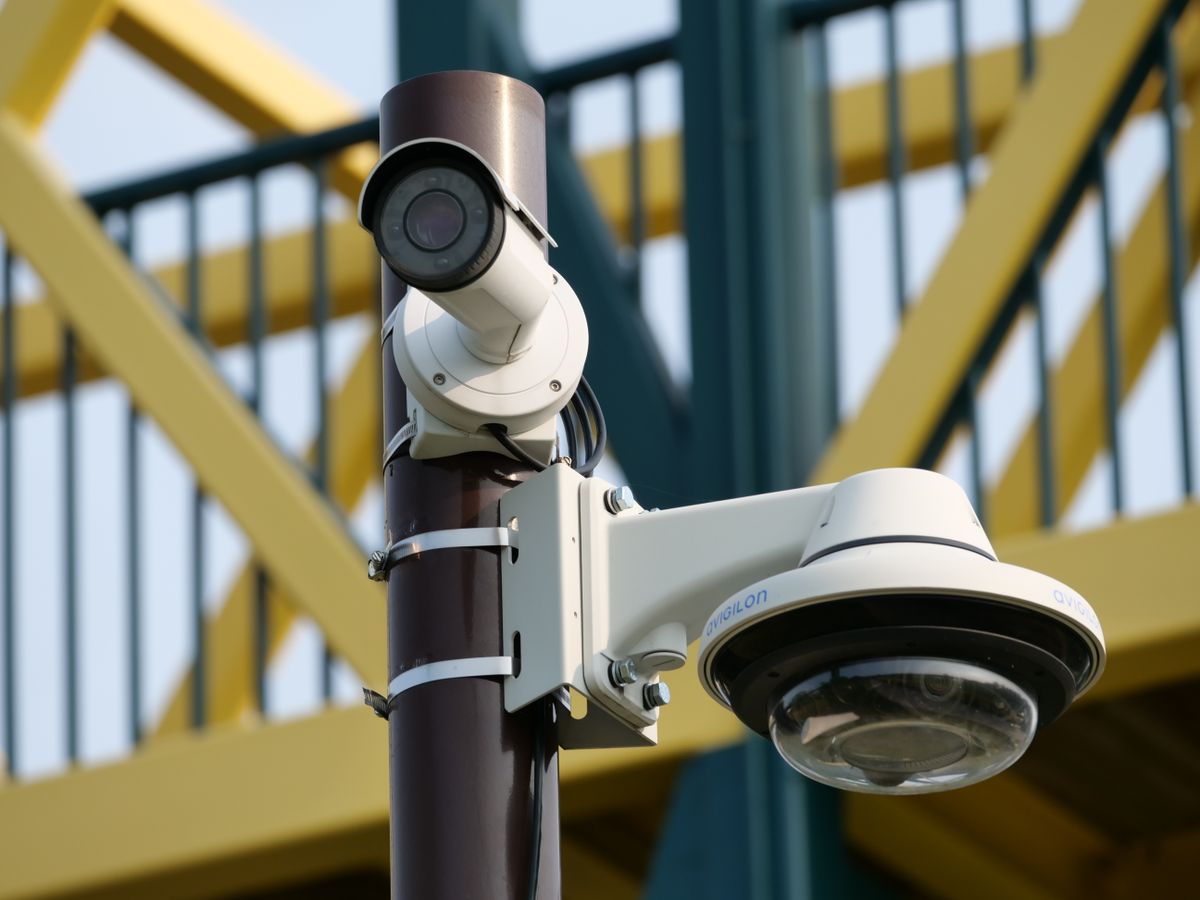 Close-up of surveillance cameras mounted on a pole against a bridge background, signifying urban safety.