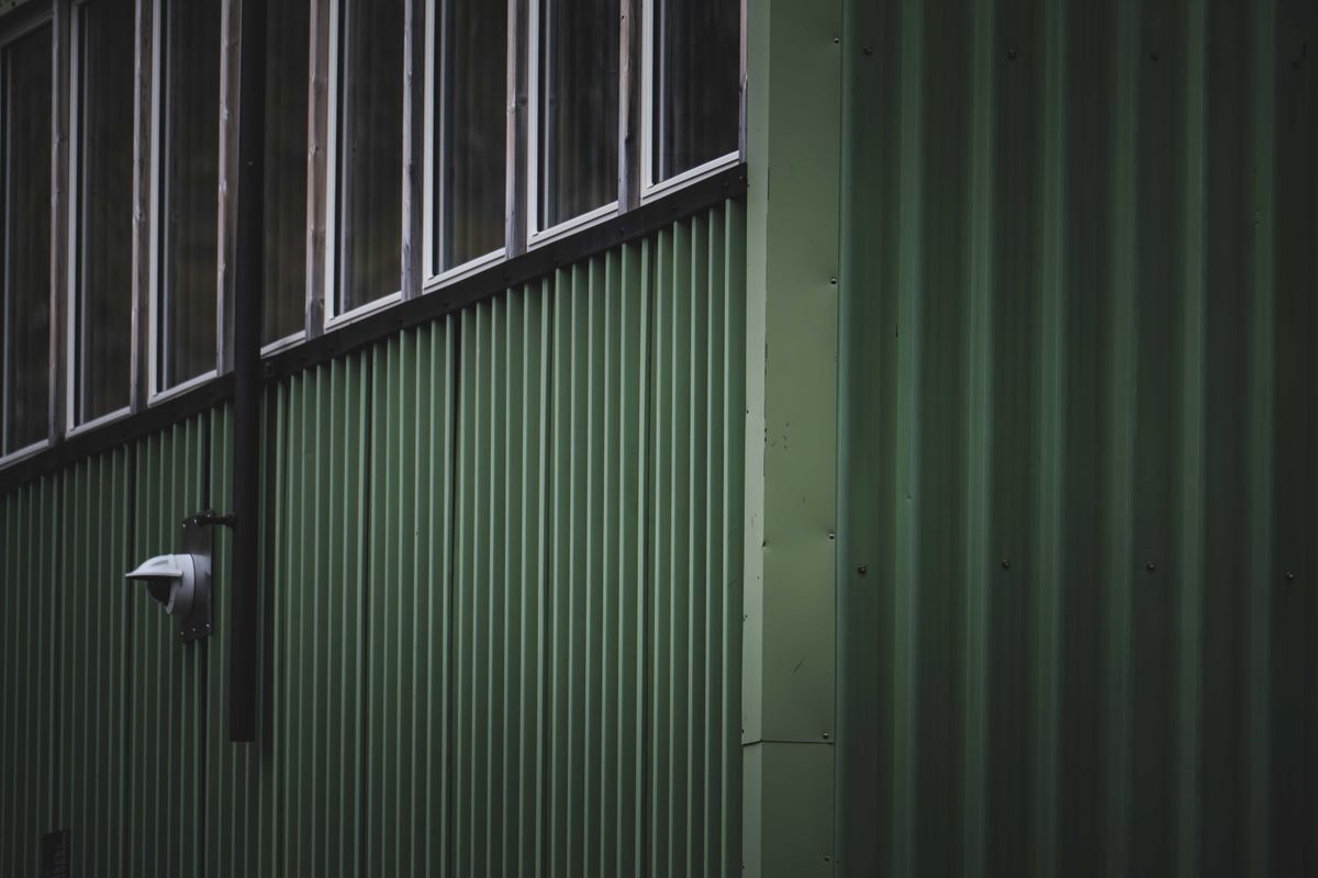Dark green corrugated metal facade with windows and security camera.