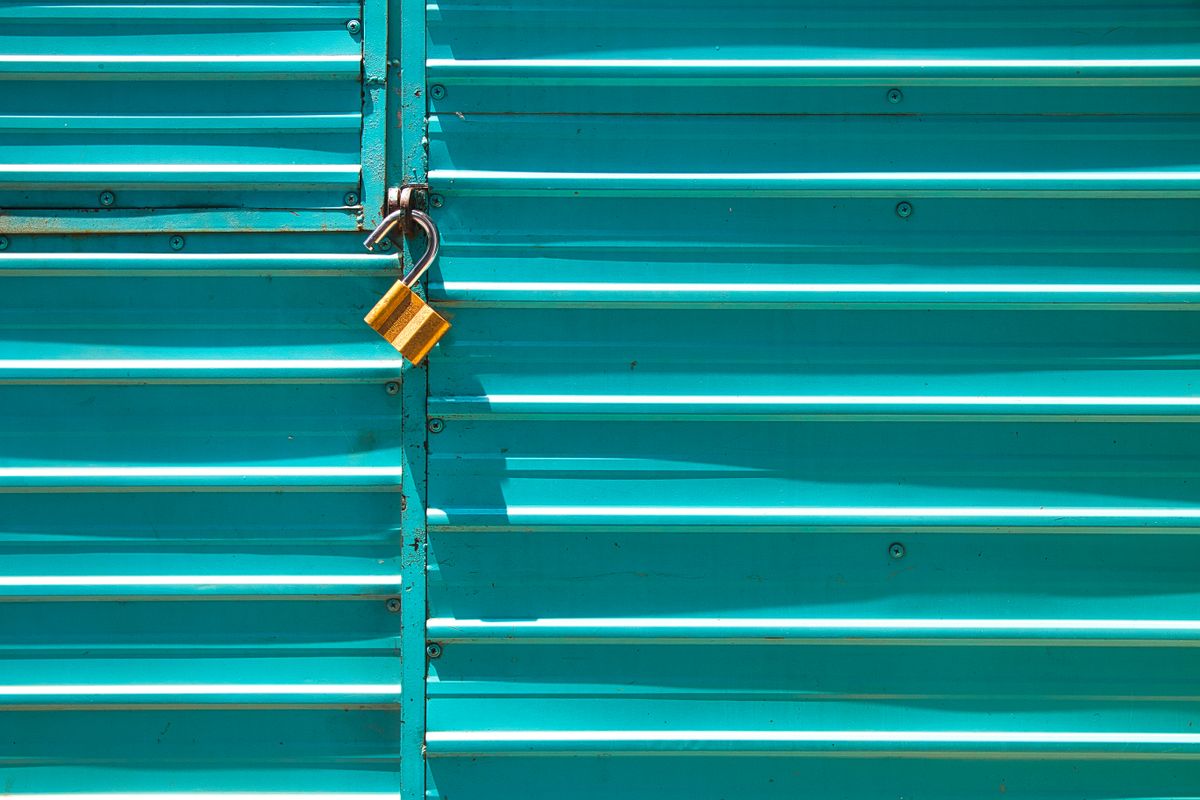 Close-up of a turquoise metal door with a golden padlock, emphasizing security.