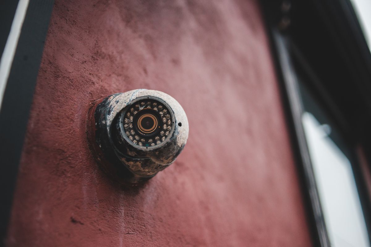 From below of aged surveillance camera with rough surface on uneven wall of house in daytime