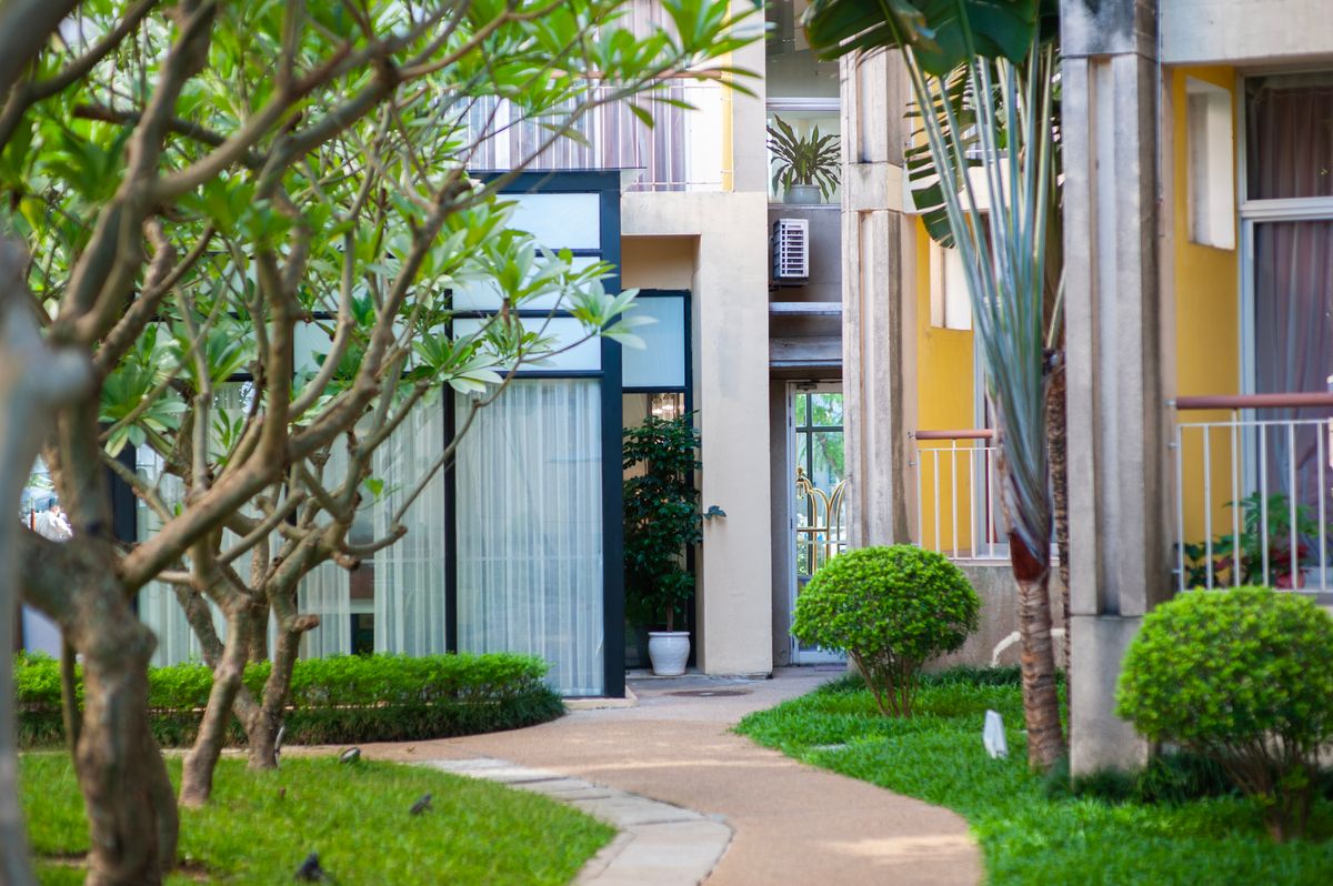 A modern apartment building with a lush garden and pathway in a vibrant setting.