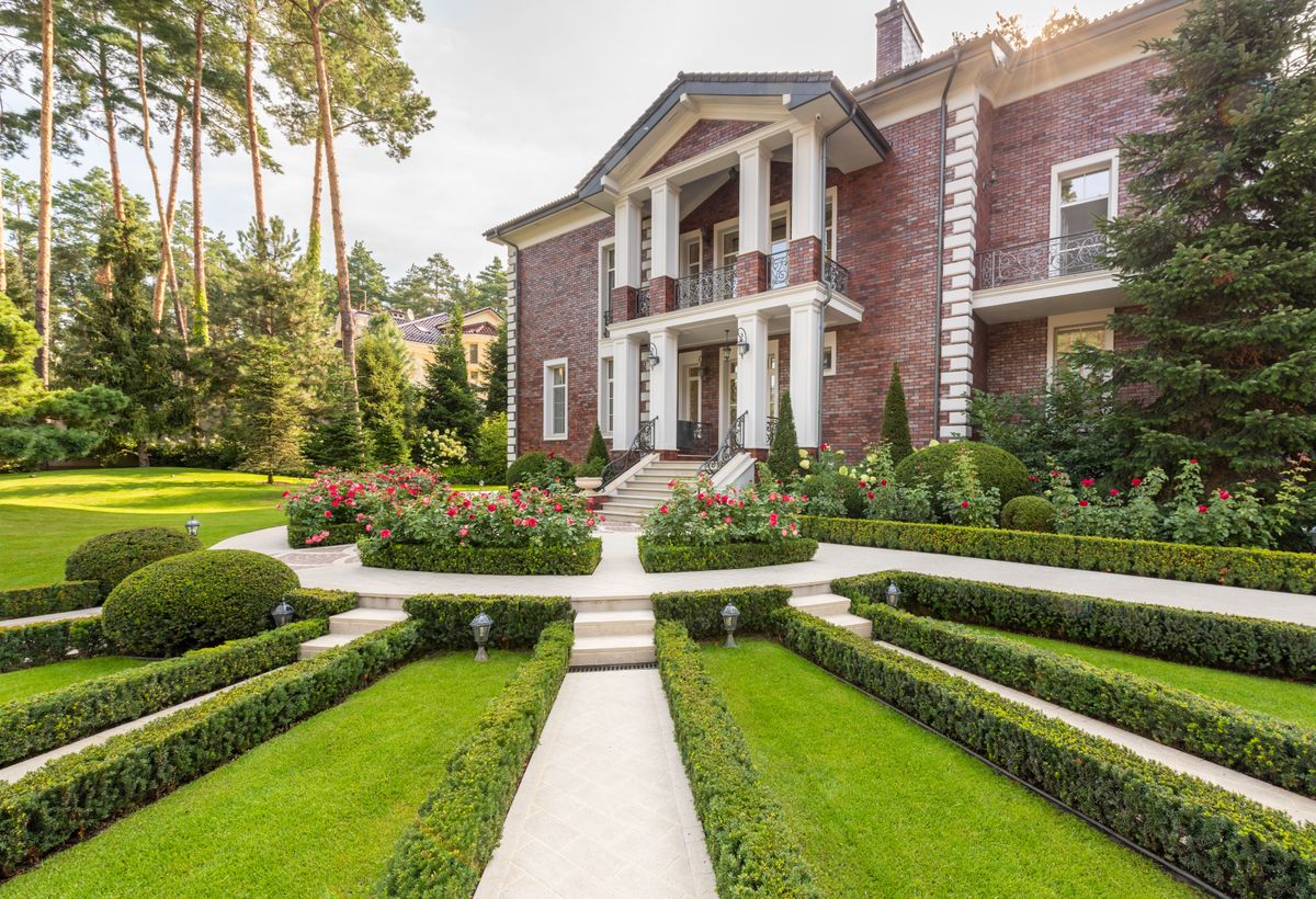Modern house near backyard with green grass and plants near trees and path under sky in summer sunny day