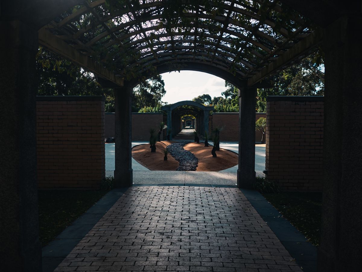 Sunlit garden pathway through brick archways and pergolas, offering a peaceful retreat.