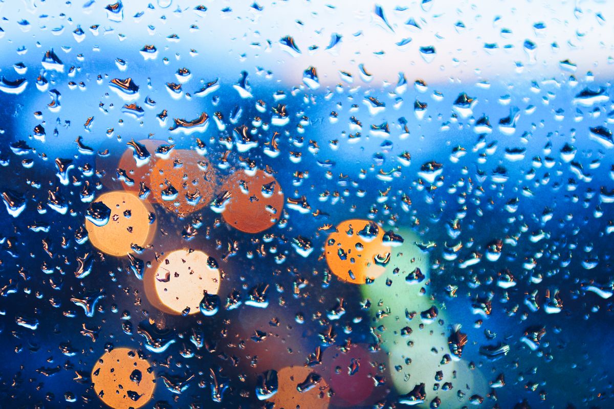 Raindrops on a window with blurred city lights create a vibrant bokeh effect at night.