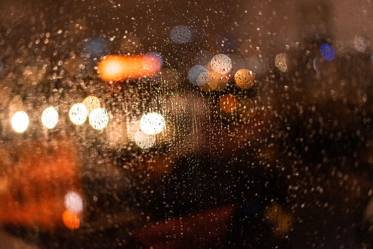 Raindrops on a window with defocused city lights creating a moody night scene.