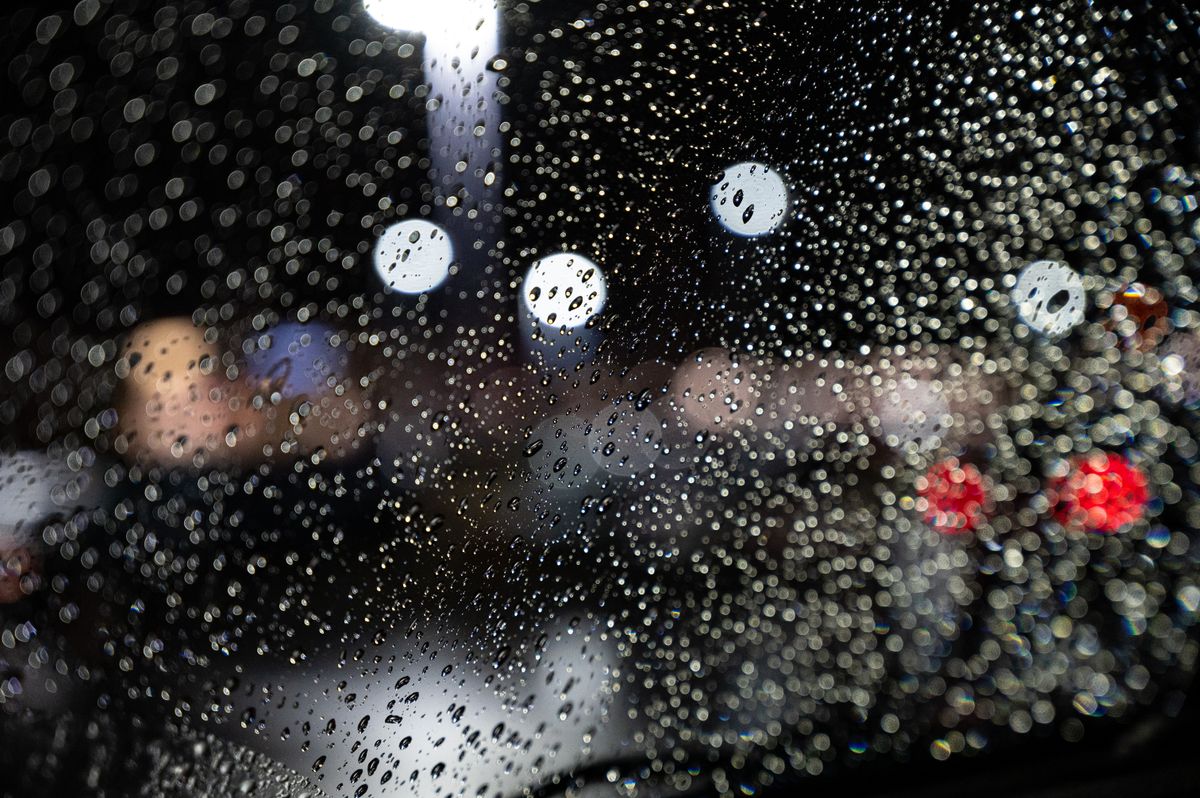 Clear raindrops on car windshield with colorful bokeh lights in the background during night time.