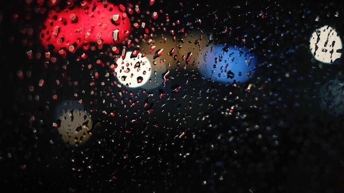 Close-up of raindrops on a window with colorful city lights bokeh at night.