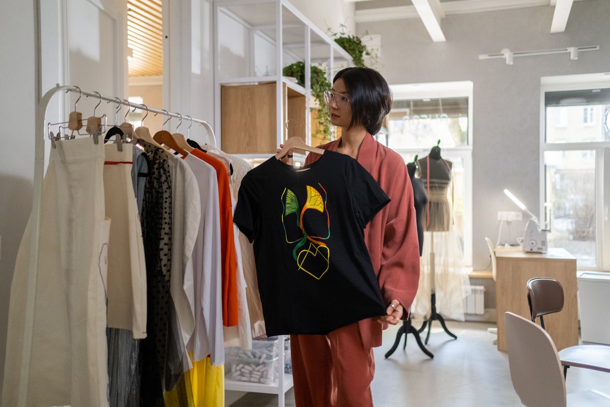 Woman in a modern studio holding a black graphic T-shirt with colorful design.