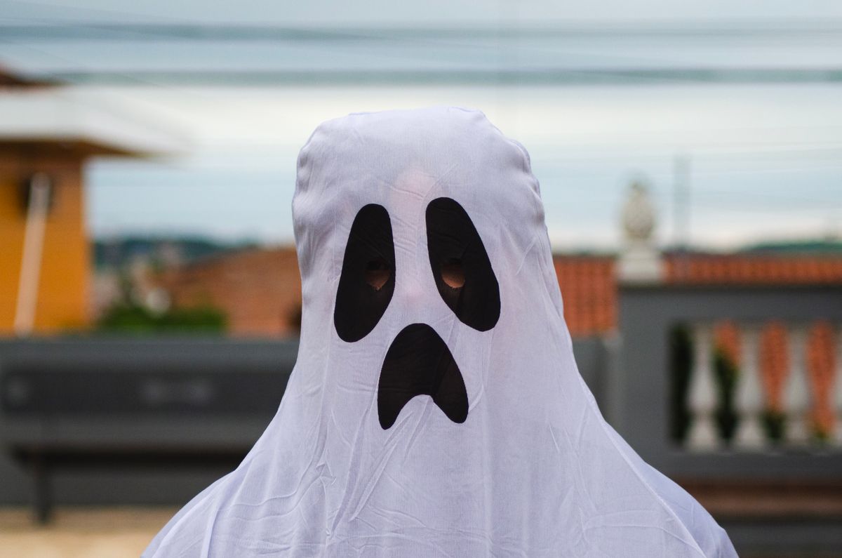 A person wearing a ghost costume with a spooky face stands outdoors.
