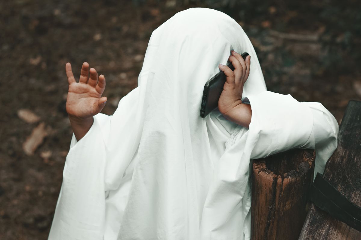 A person wearing a ghost costume makes a phone call outdoors, capturing the Halloween spirit with a playful twist.