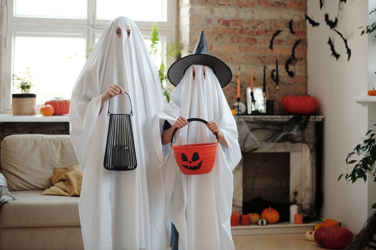 Two people wearing ghost costumes indoors with Halloween decorations. Creative DIY and spooky holiday spirit.