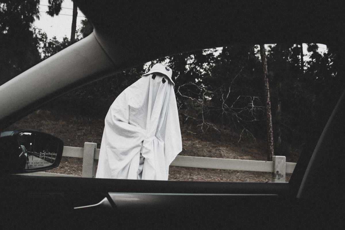 A person in a ghost costume stands by a car window, creating a spooky Halloween scene.