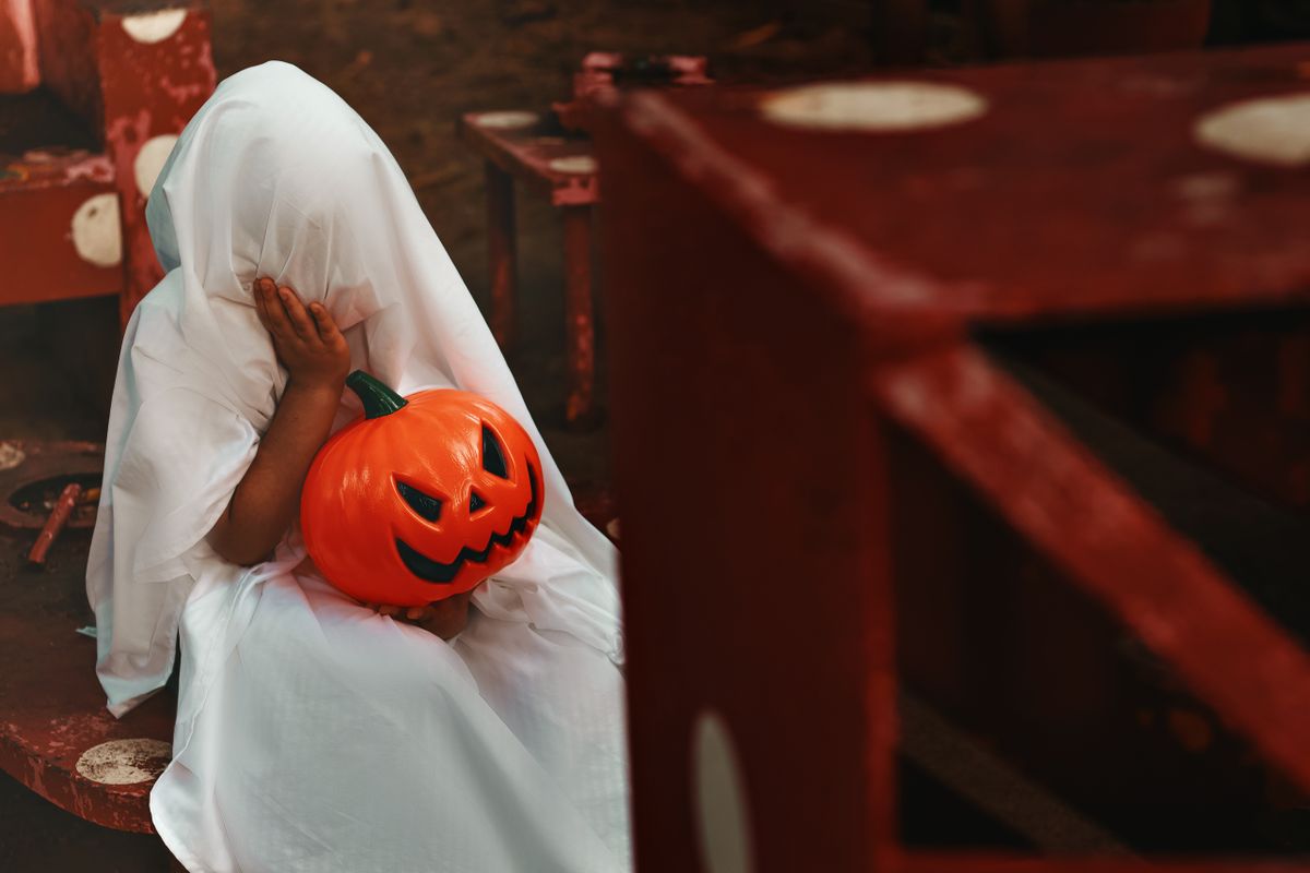 A child dressed as a ghost holding a jack o' lantern, creating a spooky Halloween atmosphere.