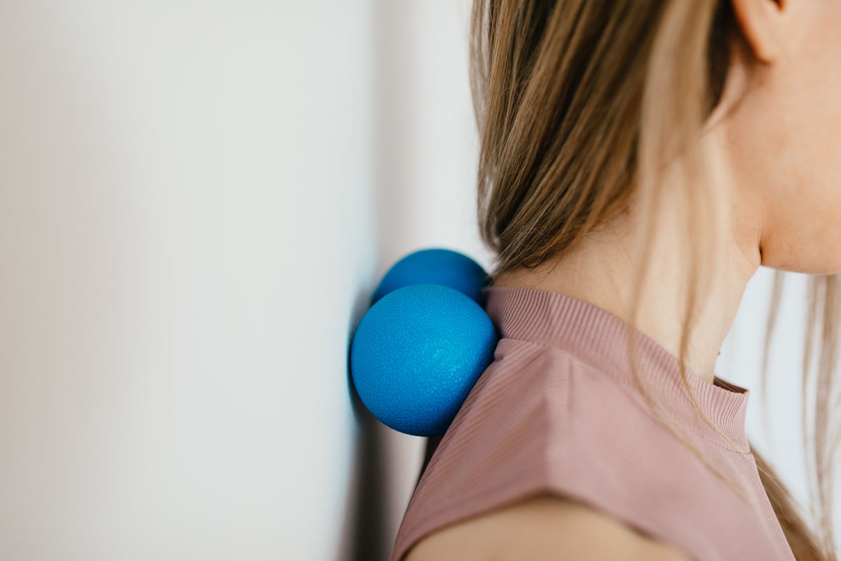 Side view crop unrecognizable female leaning on small balls against wall to massage stiff neck muscles and sore neck