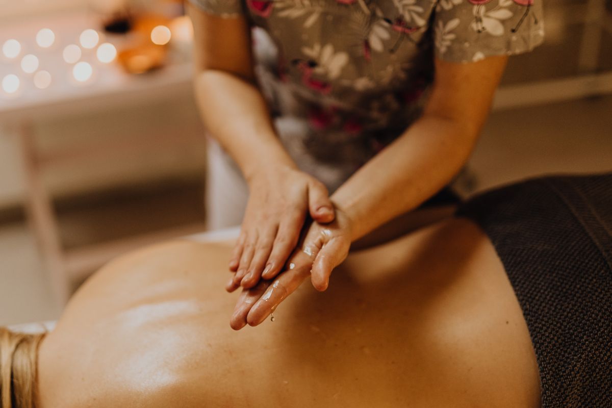 Hands massaging a person's oiled back in a calming spa setting.
