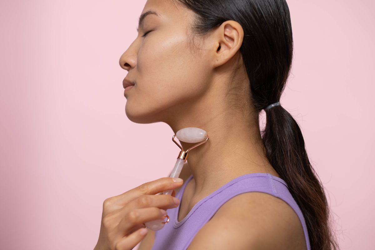 Woman using a rose quartz roller on neck for skin care and relaxation.
