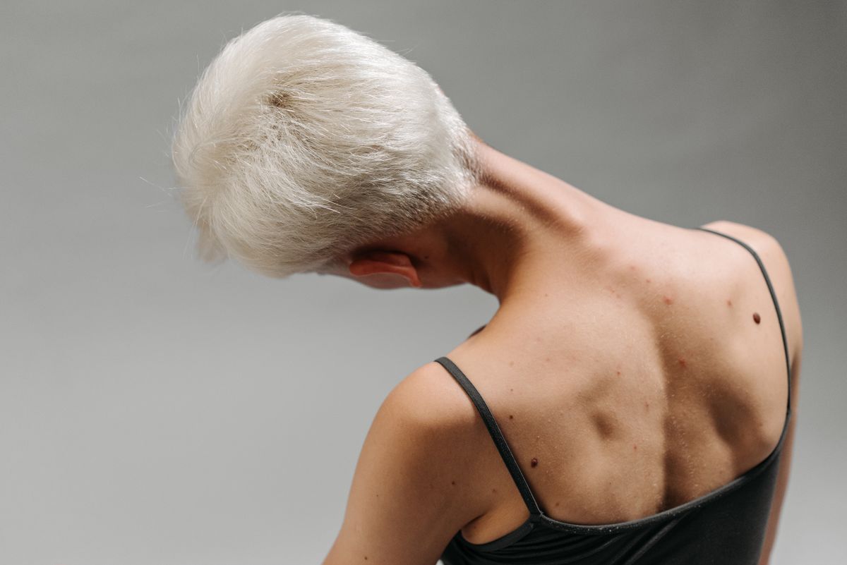 Back view of a woman with white hair bending her neck, showing body movement and detail on gray background.