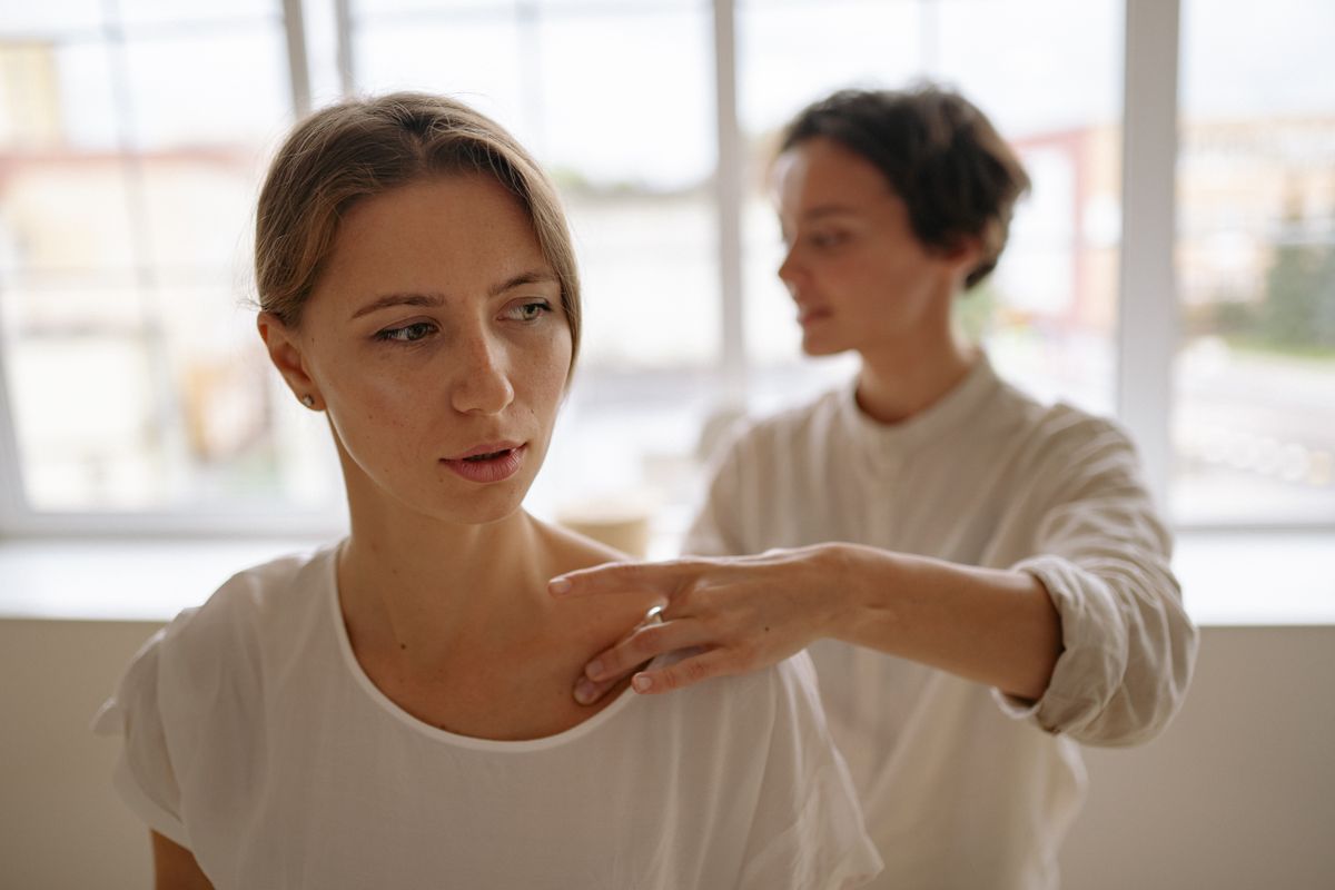 A serene spa setting featuring a therapist providing a relaxing shoulder massage to a young woman.