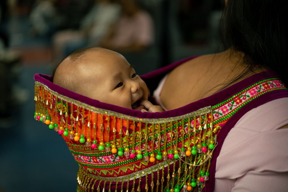 Joyful baby in vibrant traditional carrier, showcasing cultural patterns and textures indoors.