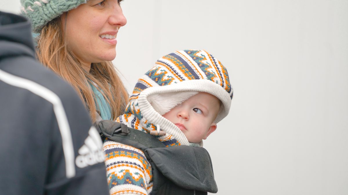 A mother carrying her baby in a cozy winter outfit, enjoying the cold season outdoors.