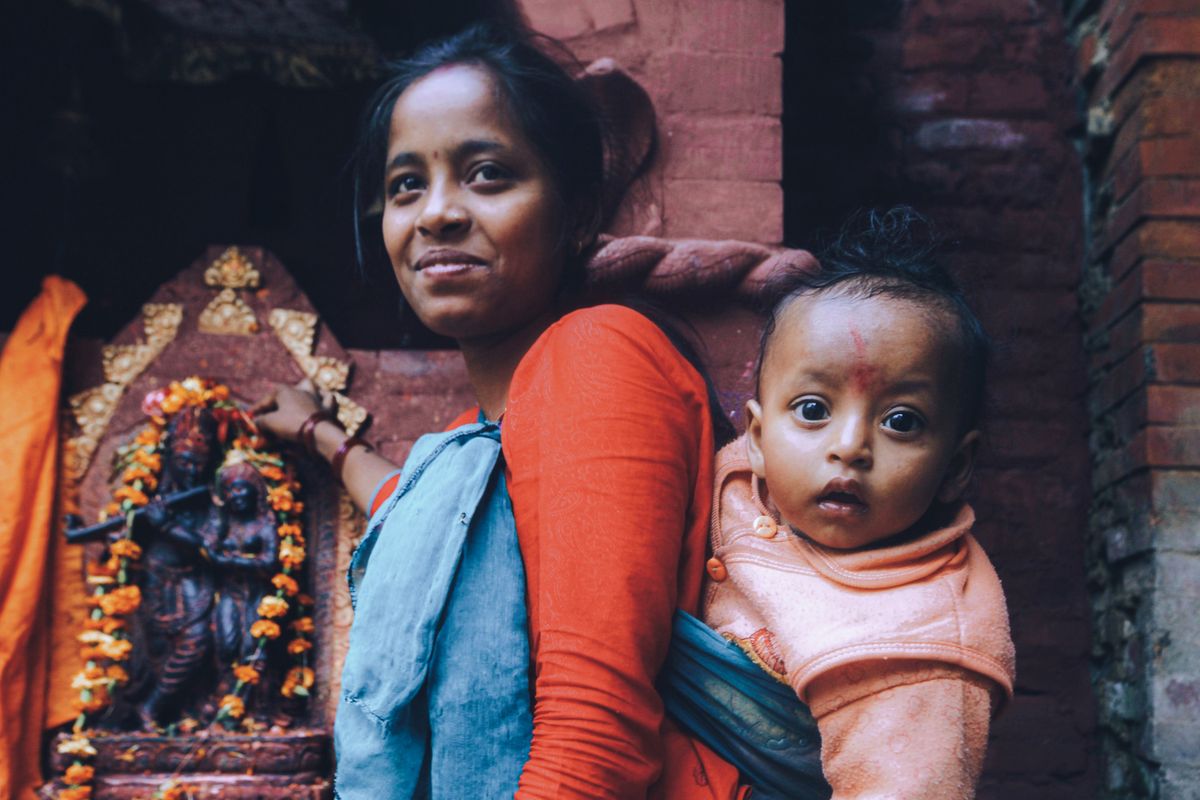 A mother and child pose near a Hindu temple shrine, showcasing cultural and religious aspects.