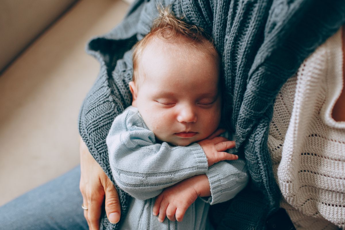 A serene and cute portrait of a newborn baby sleeping peacefully, cradled in a parent's arms.