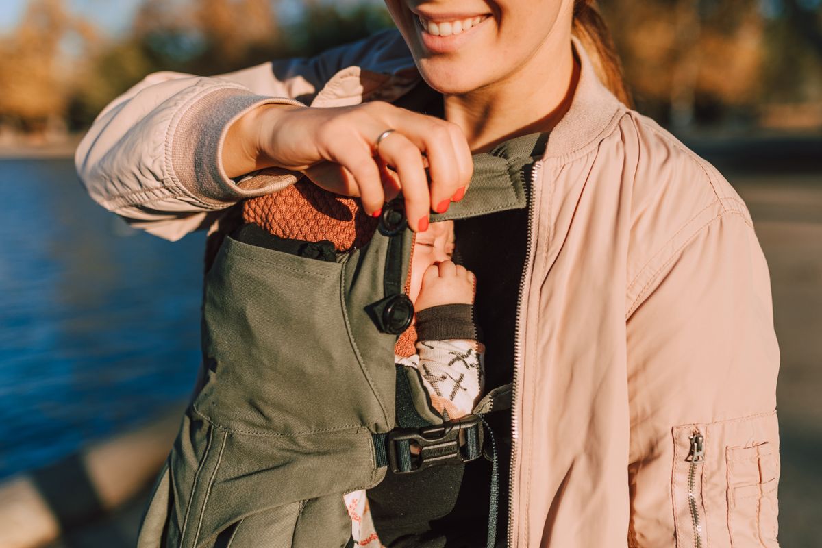 A joyful mother holds her baby in a carrier while enjoying a sunny day outdoors.