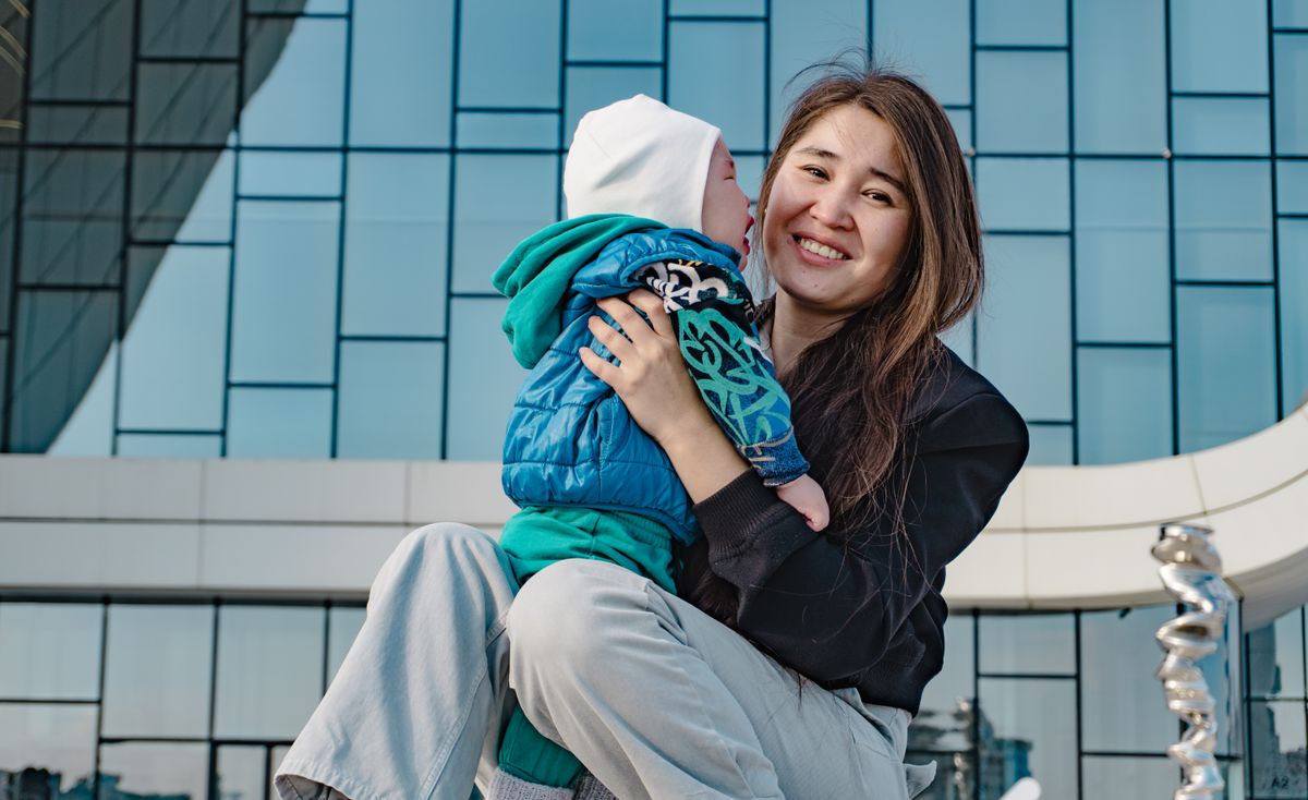 A joyful mother holding her baby outside a modern glass building, capturing a happy moment.