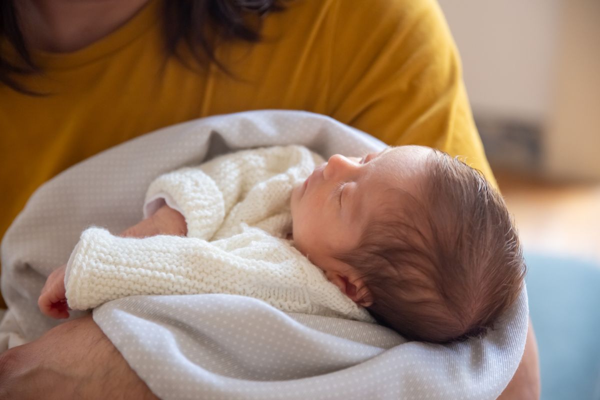 Close-up of a peaceful newborn baby sleeping in a parent's arms indoors.