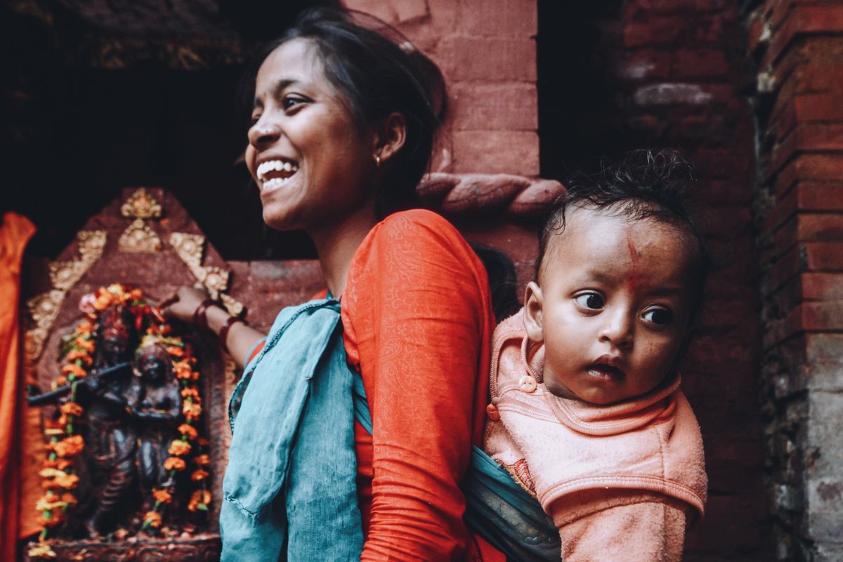 Joyful mother carrying her child near traditional Indian temple setting, showcasing happiness and culture.