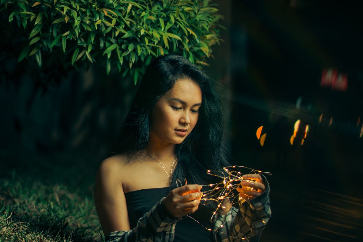 Captivating portrait of a woman holding fairy lights under a night sky, radiating a serene and magical aura.