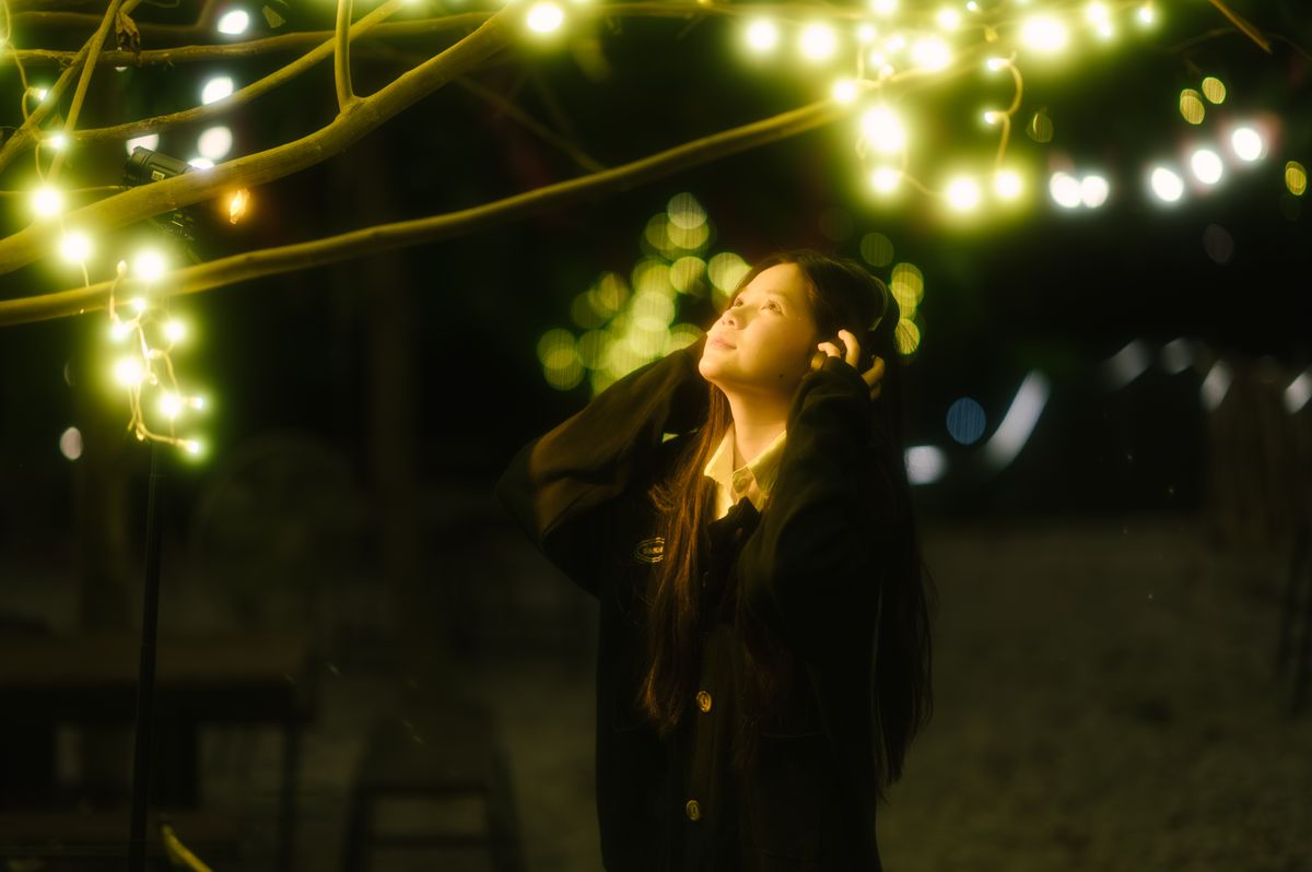 A woman gazes upwards among glowing fairy lights at night, creating a magical and serene atmosphere.