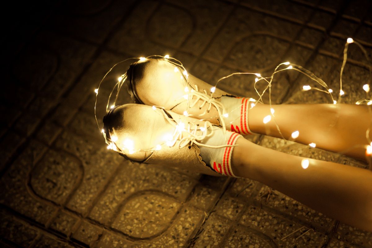 Feet in sneakers with fairy lights, creating a warm, cozy night atmosphere.