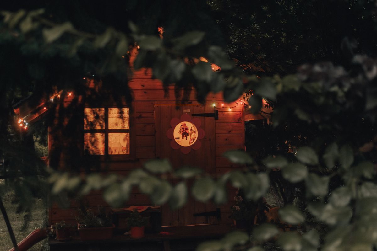 A charming treehouse illuminated at night with soft, warm lighting and surrounded by lush foliage.