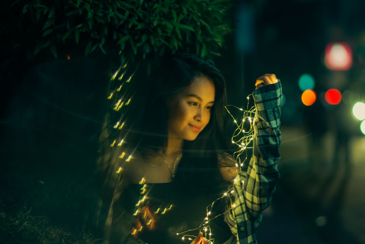 A young woman smiling while holding fairy lights on a city street at night.