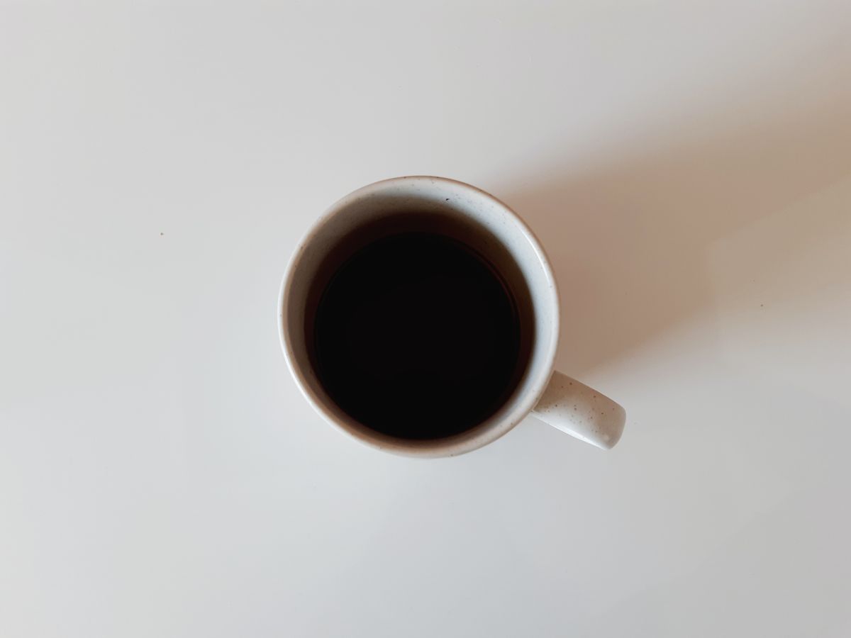 Simple ceramic mug filled with black coffee viewed from above on a white table.