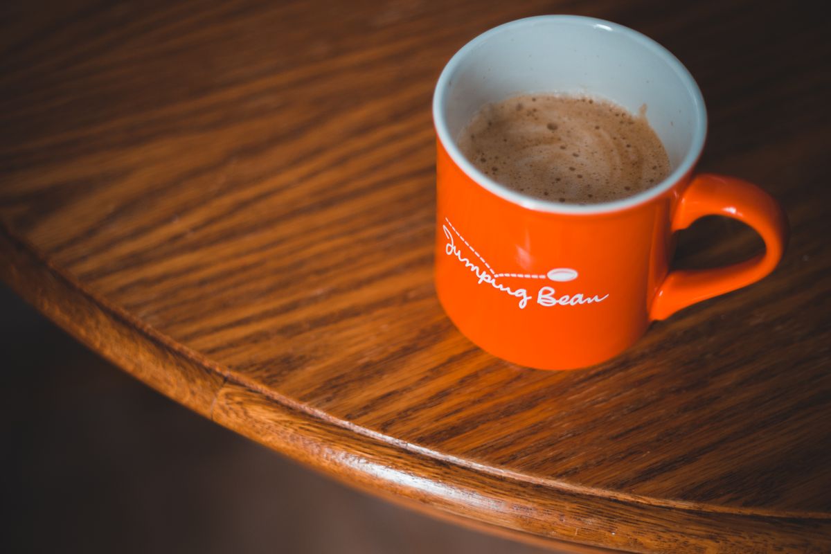 An orange mug with coffee and foam sits elegantly on a wooden table, embodying warmth and relaxation.