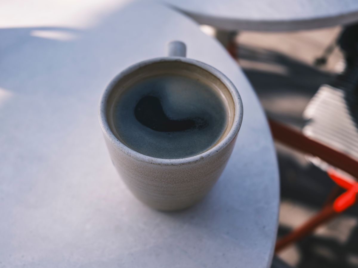 A close-up of a hot coffee cup on a sunlit outdoor table, perfect for a warm morning break.