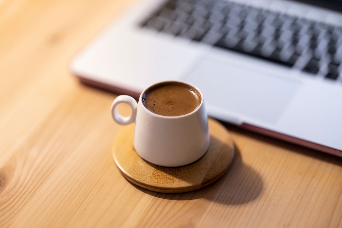 A minimalist setup featuring a coffee mug on a coaster beside a laptop on a wooden table.