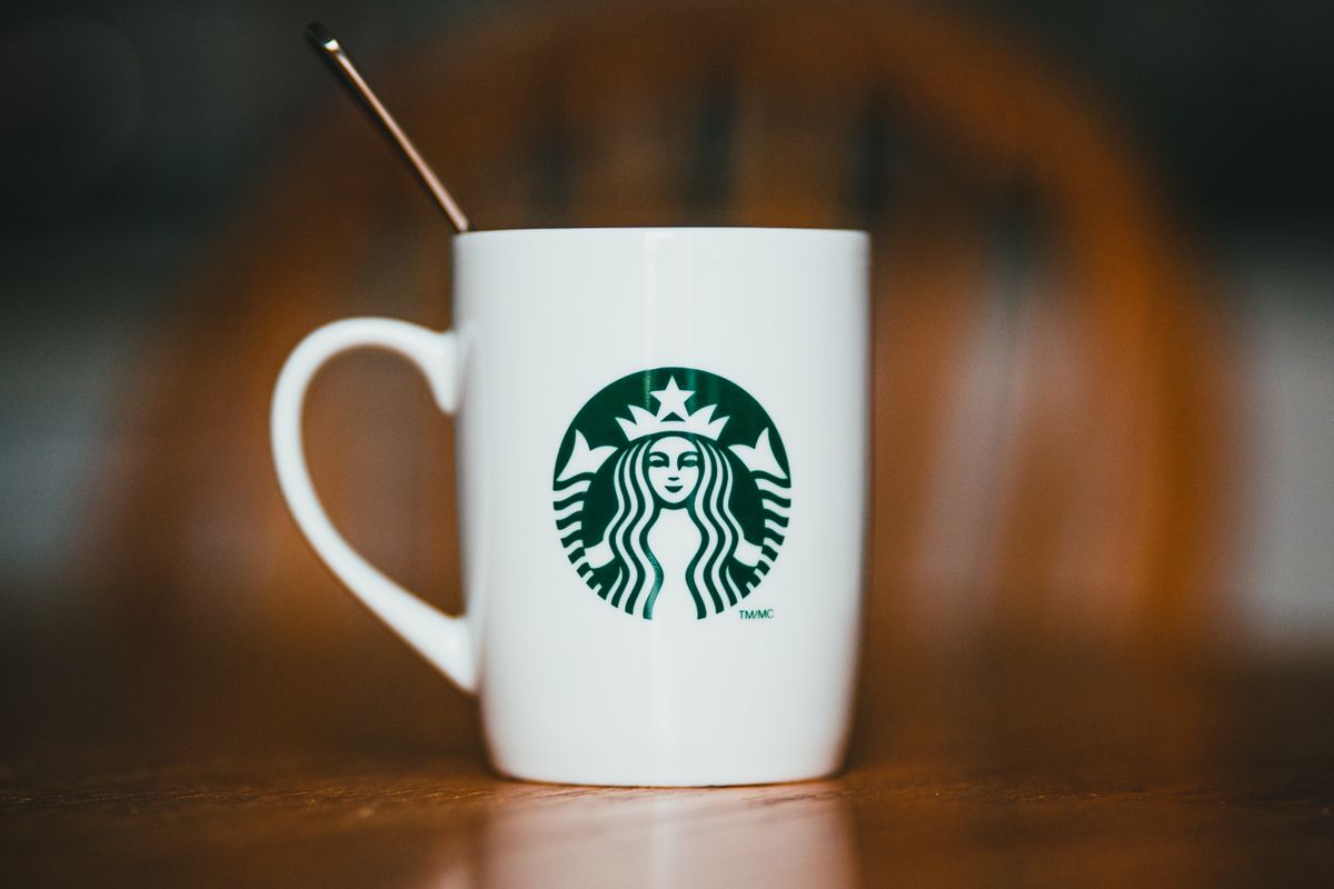 Closeup of white ceramic mug with logotype of brand with hot drink and teaspoon placed on wooden table