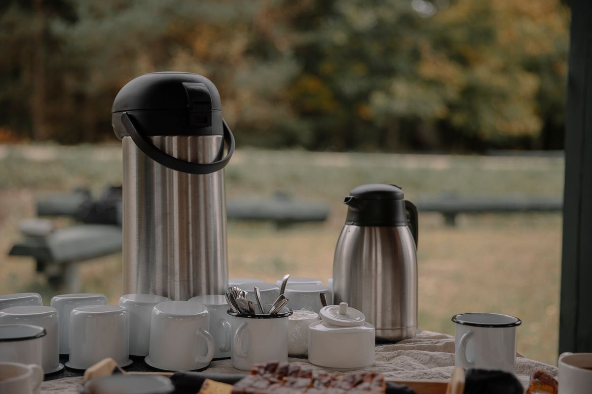 A cozy outdoor coffee setup with thermos, cups, and snacks on a table, perfect for group gatherings.