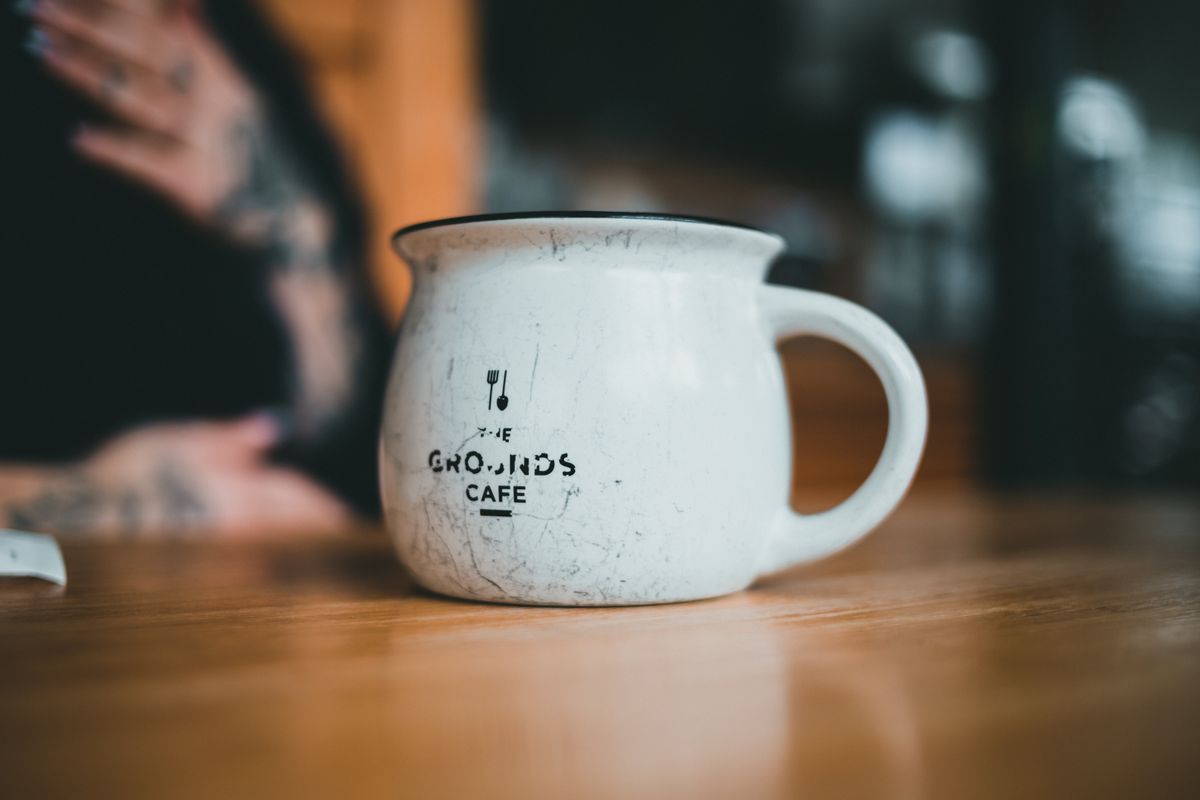 A vintage-style ceramic coffee mug with logo, placed on a wooden table with a blurred background.