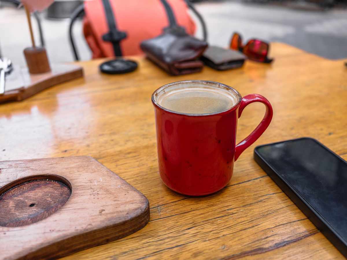 A cozy café setup with a red coffee mug and smartphone on a wooden table.