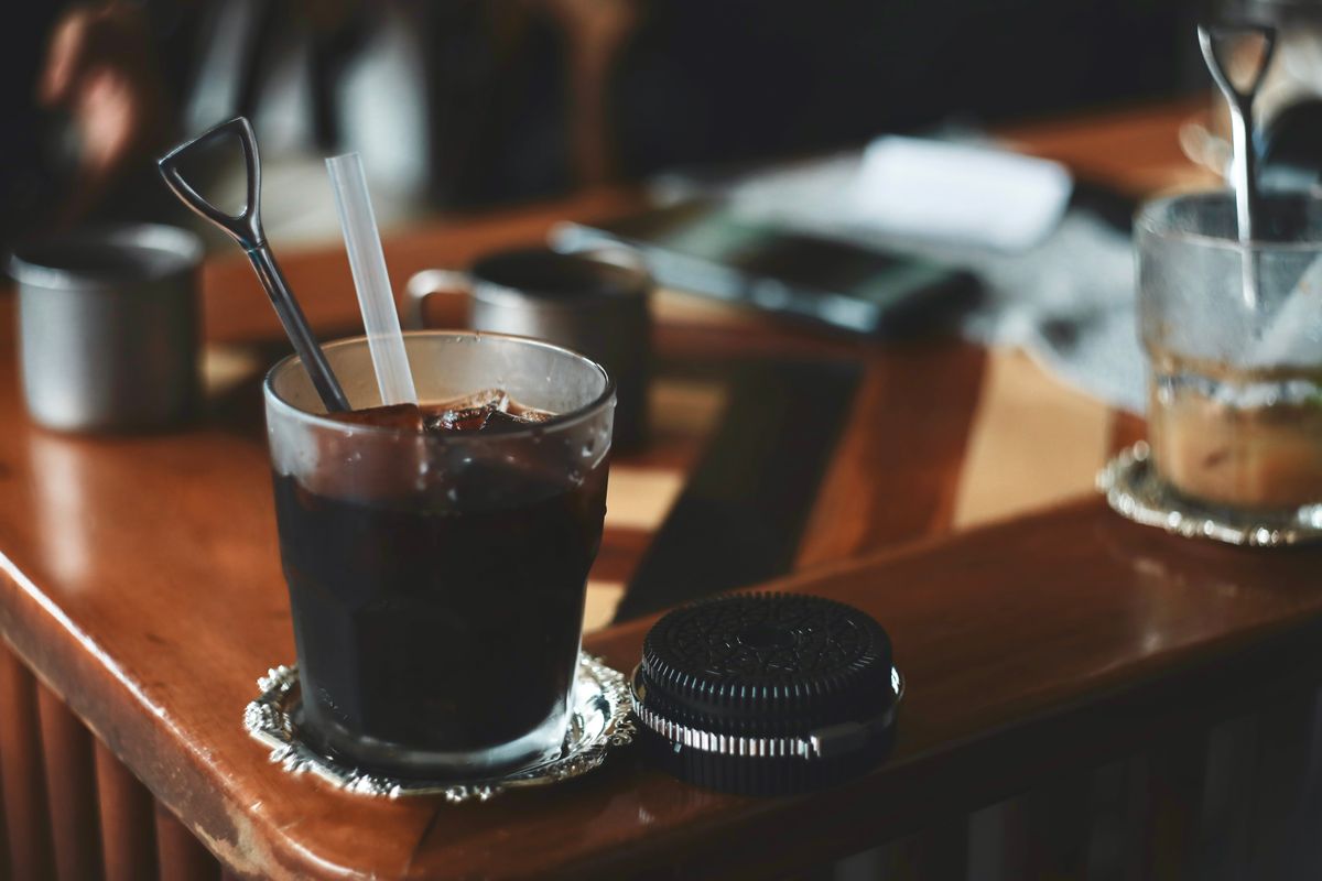 Chilled iced coffee served in a glass with metal stirrer on a cozy wooden table.